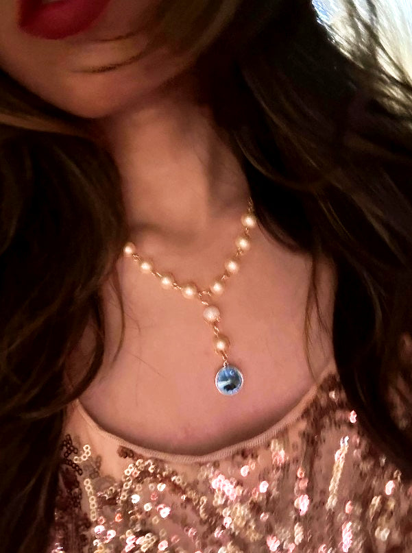 Girl wearing a pearl necklace with a blue pendant and a sequined dress, evoking Old Hollywood glamour.