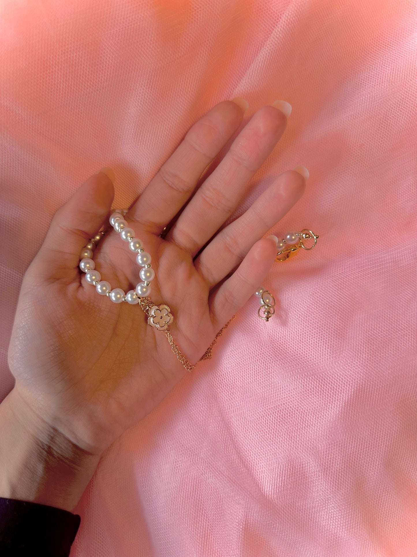 The Emery necklace resting in the palm of a hand, emphasizing the intricate floral pendant and smooth pearls up close.