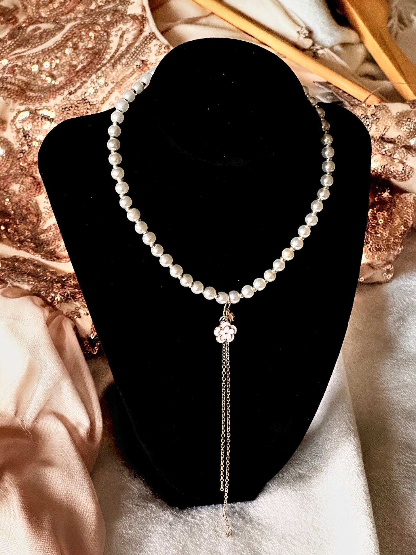 The Emery necklace displayed on a black mannequin, showcasing its lustrous white pearls, delicate floral pendant, and elegant gold chain tassel.