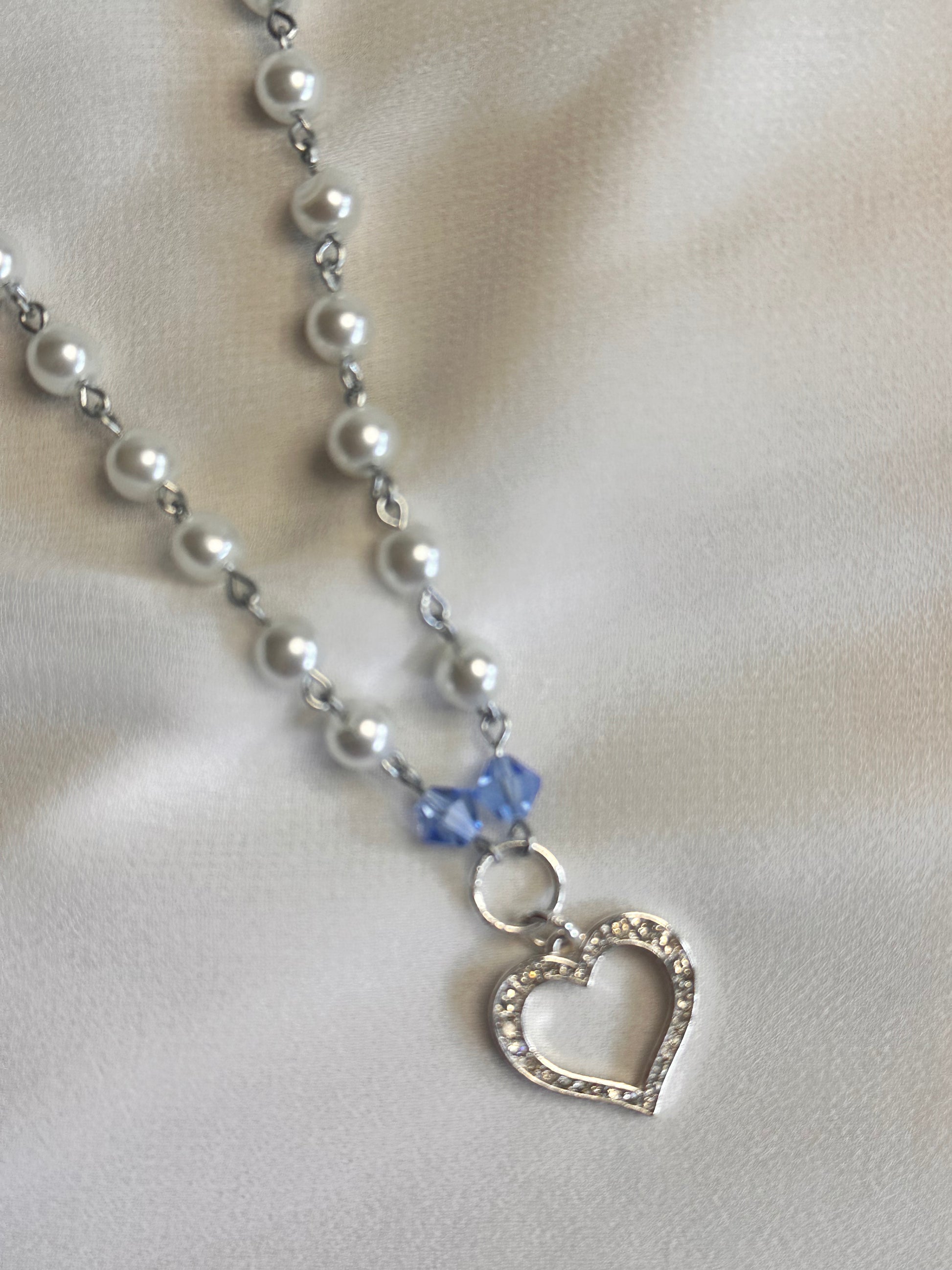 Close-up of the Cinderella Necklace's heart charm and faux pearls, laid out on soft fabric.