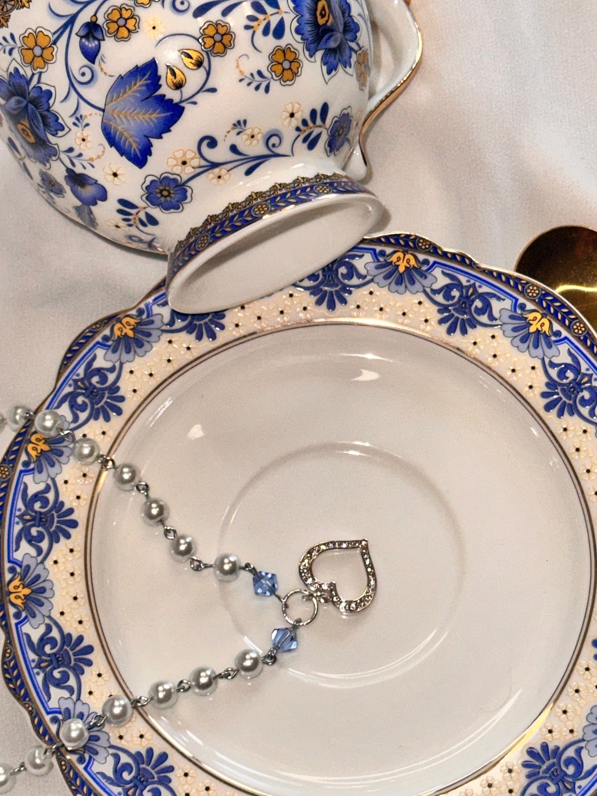 Cinderella Necklace with a Sterling Silver heart charm displayed on a decorative plate beside a matching teapot