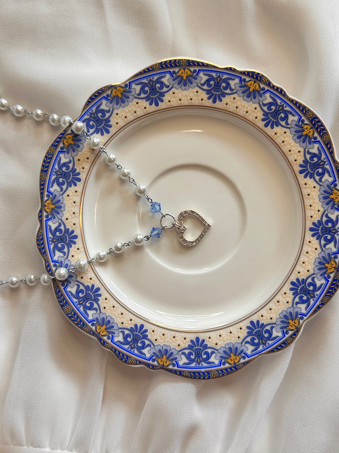 Cinderella Necklace elegantly displayed on a plate, captured from a different angle with a vintage teacup in view.