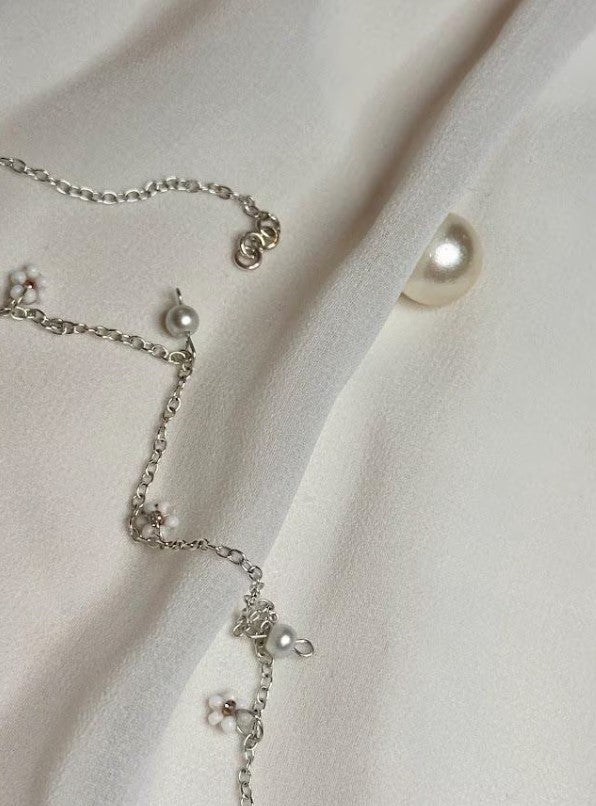 Teatime Necklace laid out on soft fabric, highlighting the delicate silver chain and pearls.